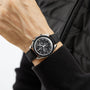 A person wearing an OMEGA Speedmaster Moonwatch Professional with a black strap and a black quilted jacket.