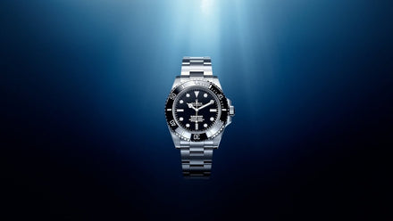 A silver luxury wristwatch with a black face is illuminated against a dark blue gradient background.