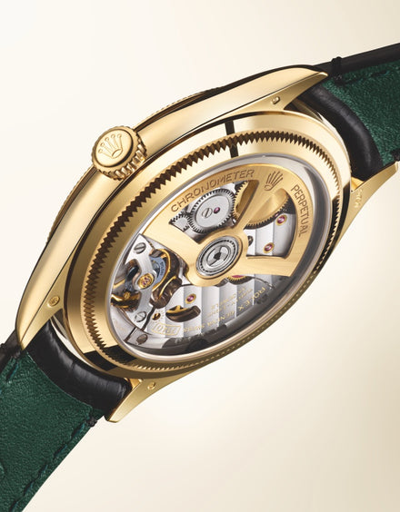 Close-up of a gold watchs movement with Chronometer Perpetual text, green leather strap, and black stitching.