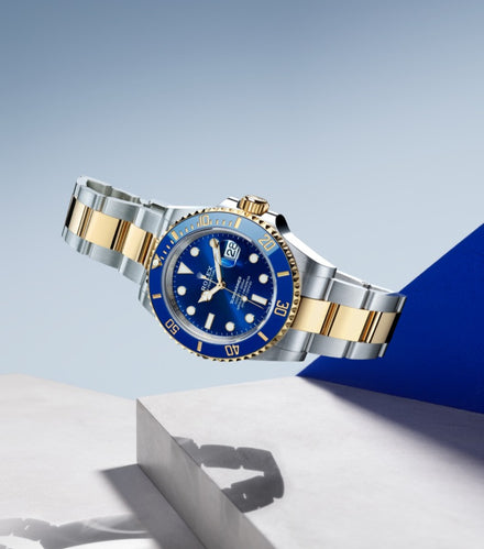 Luxury two-tone wristwatch with a blue face and gold accents displayed on a white geometric surface.
