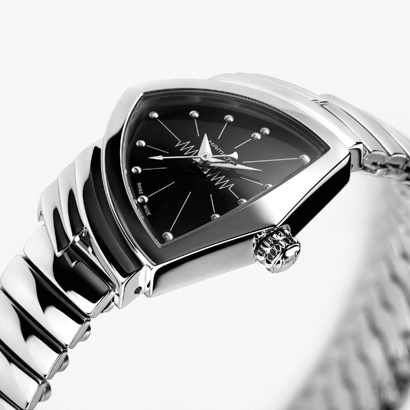 A close-up of the Hamilton Ventura S Quartz shows its silver case, black triangular dial with metallic hour markers, zigzag pattern, and a sleek metal link band inspired by Mid-Century Modern design.