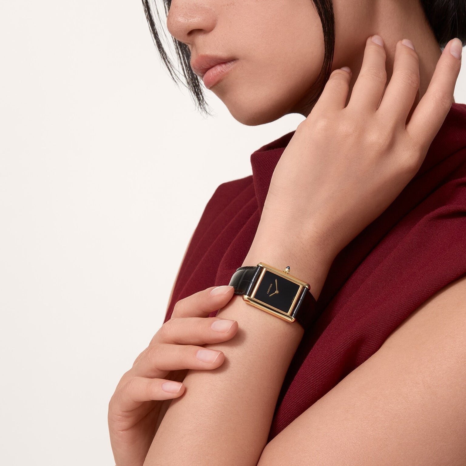 Person wearing a sleeveless burgundy top and a Cartier Tank Louis Cartier black and gold square watch, touching their neck.