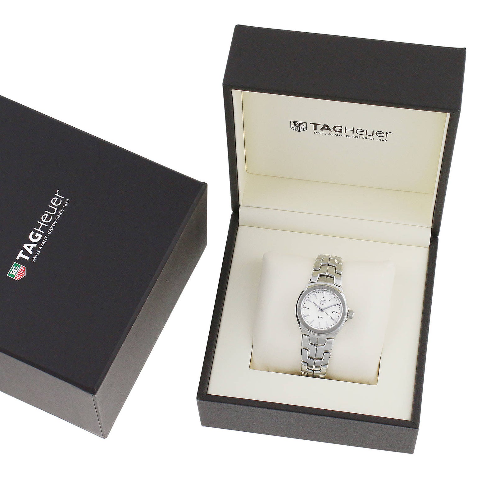 A TAG Heuer Link Date silver wristwatch with a mother-of-pearl dial is displayed in an open branded box, with the black outer box beside it.