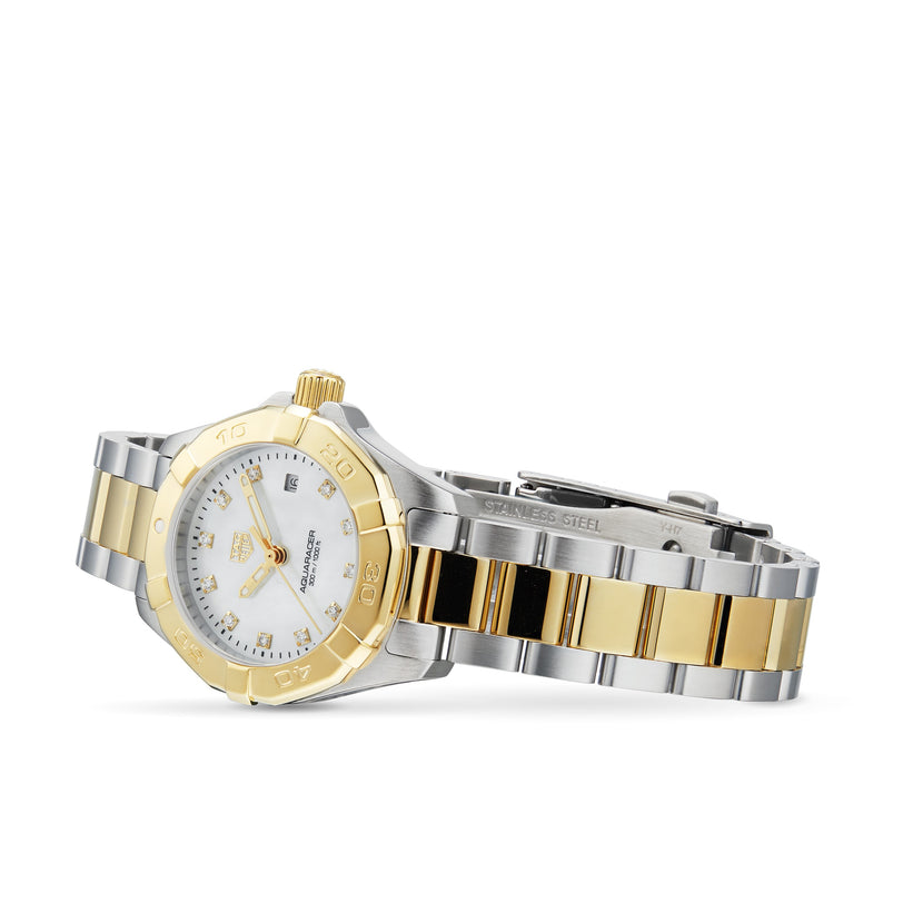 The TAG Heuer Aquaracer Date, a two-tone wristwatch in stainless steel and 18K gold with a white dial, date display, and metal link bracelet, is elegantly displayed on its side against a white background.