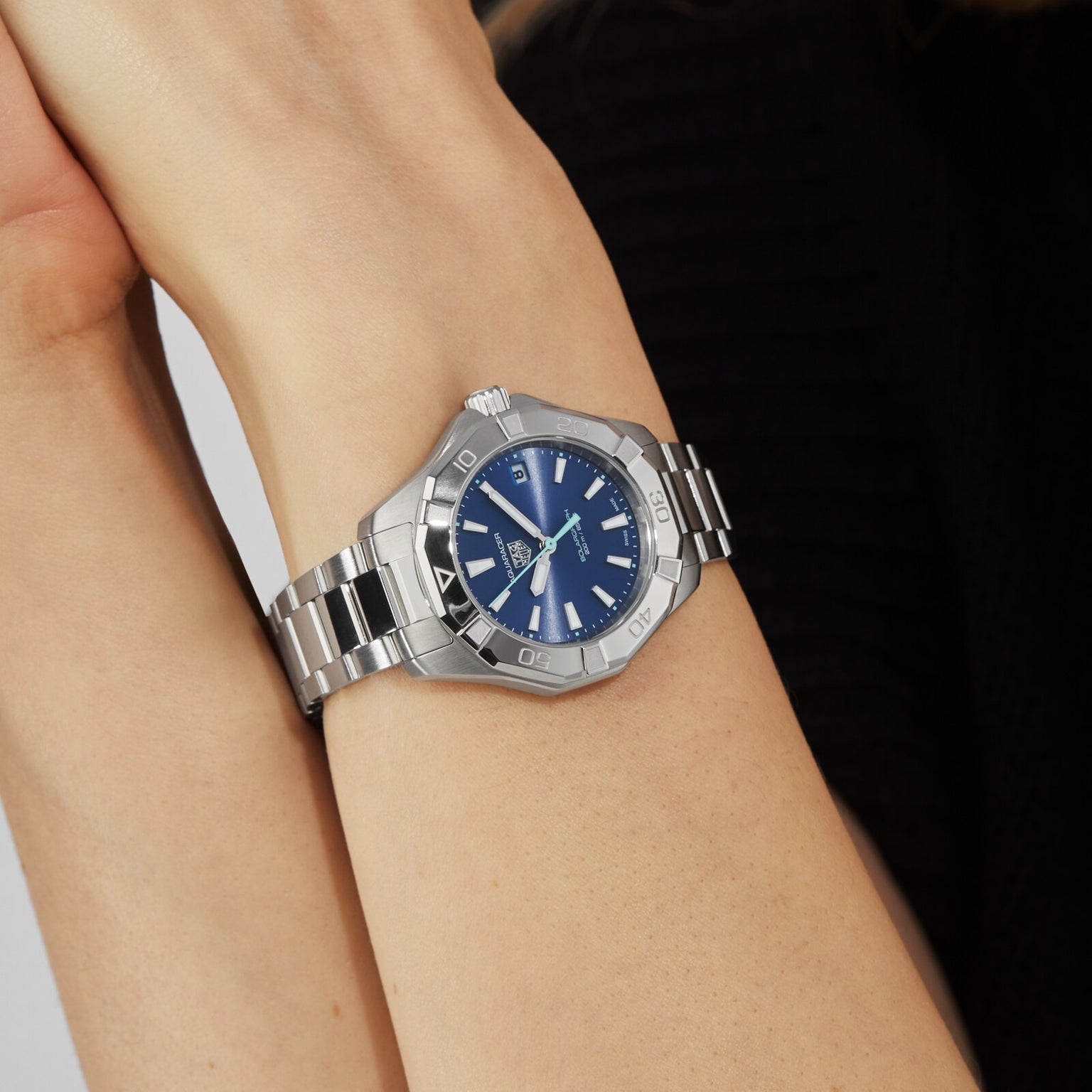 A person wears a TAG Heuer Aquaracer 200 Professional Solargraph with a silver metal band and blue face, displayed on their wrist against a plain background.