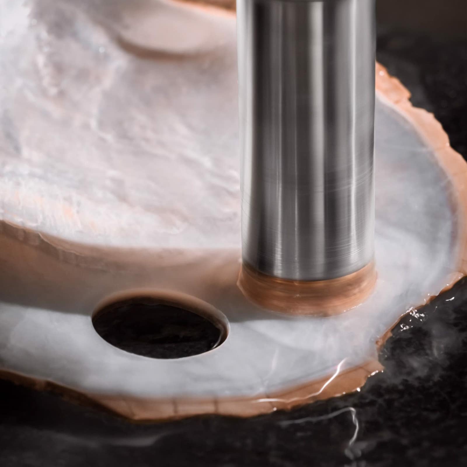 A close-up of a hole being drilled into a translucent shell evokes the intricate craftsmanship behind the Vacheron Constantin Traditionnelle Moon Phase watch.