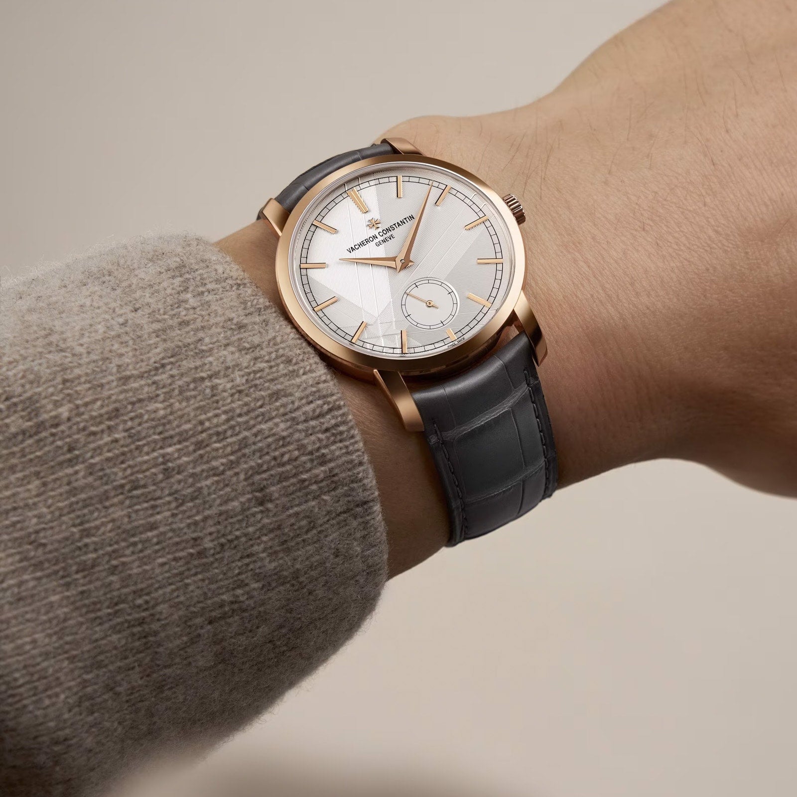A person wearing a Vacheron Constantin Traditionnelle Manual-winding watch with a white dial, 18K pink gold accents, and a black leather strap.
