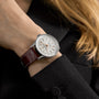 A person in a black blazer showcases the Breitling Navitimer Automatic 36, featuring a silver-toned white dial, brown leather strap, and a 36mm stainless steel case.