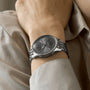 A person wearing a Breitling Navitimer Automatic 36 with a silver metal band and grey dial, paired with a beige long-sleeve shirt.