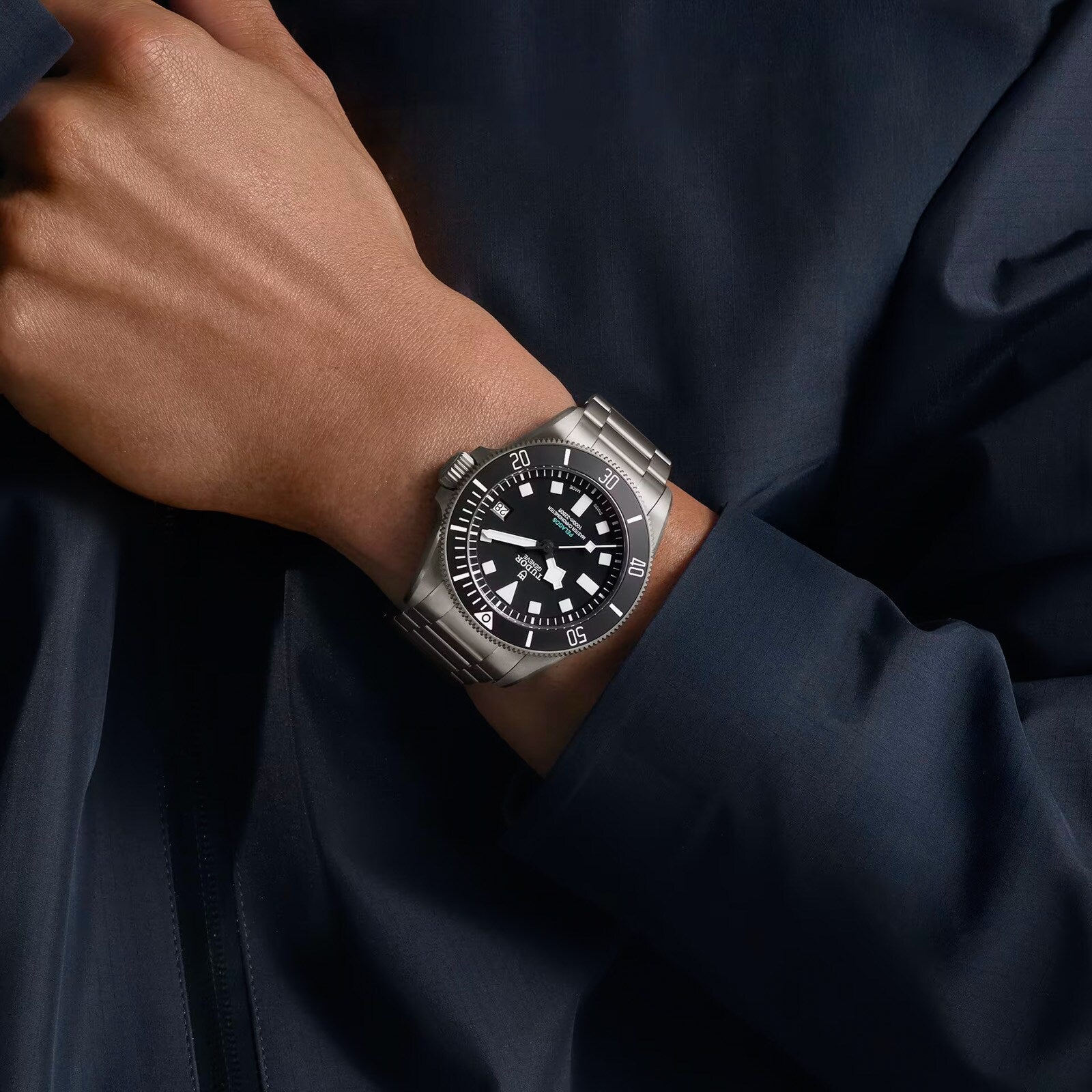 A person wearing the TUDOR Pelagos Ultra, a silver dive watch with a black dial and white markers, on their wrist.