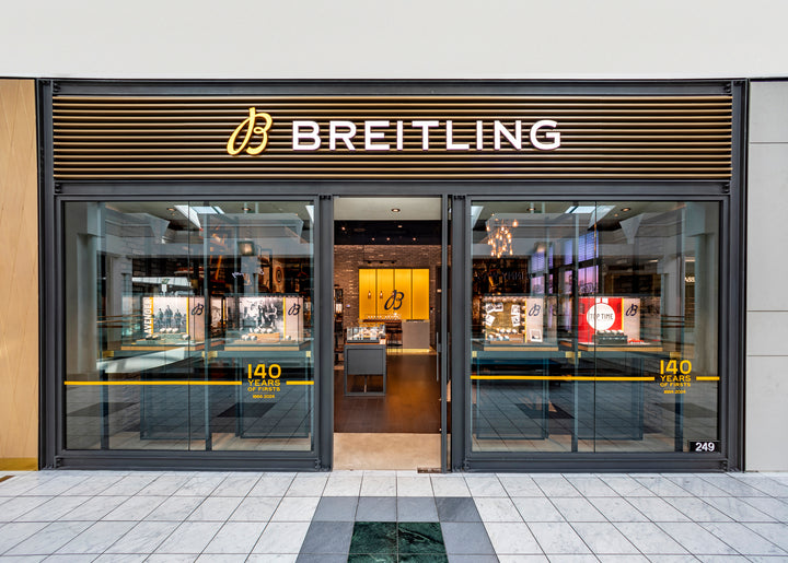 Storefront of Breitling with glass doors, watch displays, and 140 Years sign on the entrance.