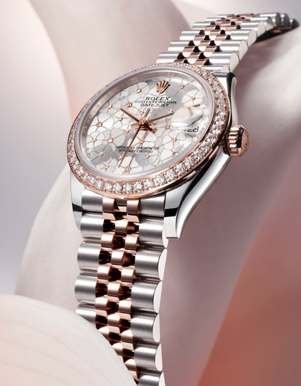 A luxury Rolex watch with a silver and rose gold band, diamond bezel, and textured dial, displayed elegantly.