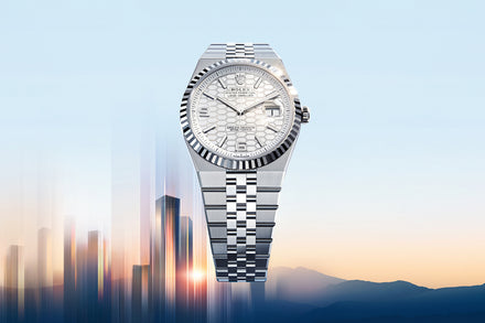 A silver Rolex watch with a patterned face is displayed over a cityscape at sunrise.